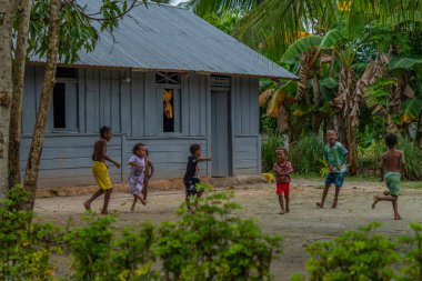 Raja Ampat, Batı Papua, Endonezya, Şubat 06.2023: Raja Ampat 'ta oynayan yerli papualı çocuklar, arka planda mavi bir ev