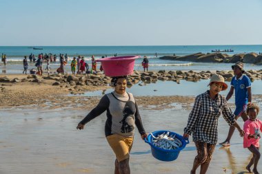 Morondava, Madagascar - May 31.2023: Two madagasy women with painting, known as Masonjaony, carry fish at the coastline from Morondava