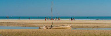 Coastline from Morondava with a baobab wood boat at low tide on sand, background with people panorama
