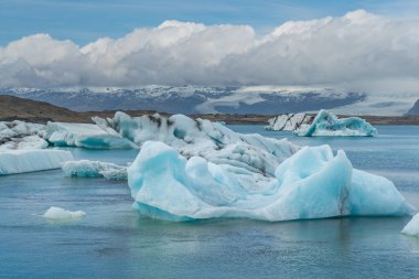 Joekulsarlon Buzul Gölü Güney İzlanda 'da mavi buzla kaplı arka planda karla kaplı bir dağ sırası