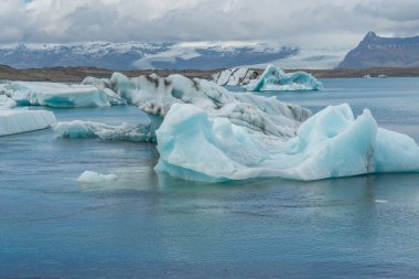 Joekulsarlon Buzul Gölü Güney İzlanda 'da mavi buzla kaplı arka planda karla kaplı bir dağ sırası