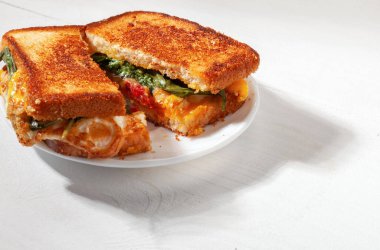 Lezzetli ev yapımı, kızarmış yumurta, erimiş peynir, domates dilimleri ve fesleğen yapraklı ev yapımı sandviç.