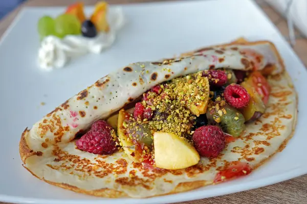 Dessert plate. Pancake with fruit mix, pistachio nuts and raspberry jam topping