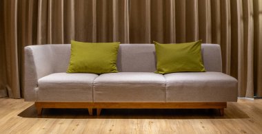 Çağdaş bir odada, kahverengi deri döşemeli ve yumuşak yastıklı kanepe, perde arkasına yaslanmış, rahat ve şık bir iç mekan yaratıyor.