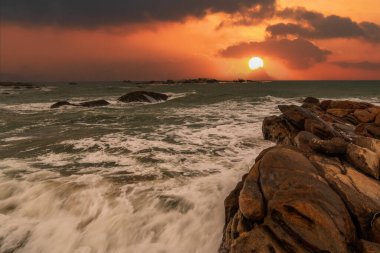 Okyanusun üzerinde güzel bir gün batımı. Önünde kayalar var.