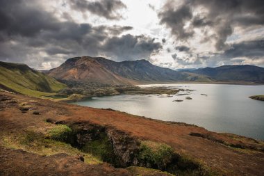 İzlanda 'da renkli bir arazide bir tepenin kenarında yürüyen yürüyüşçüler.
