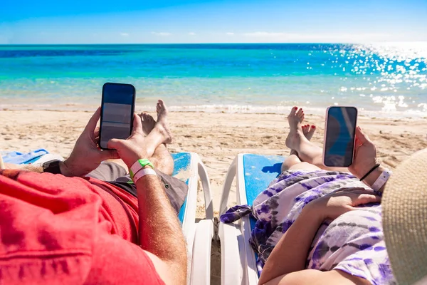 해변에서 휴식을 취하고 부부는 의자에 휴가를 즐기면서 핸드폰을 — 스톡 사진