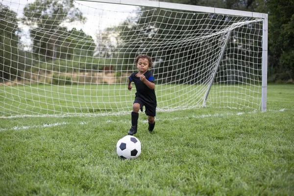 大きな芝生のフィールドでサッカーの試合中にゴールからボールを蹴り若いアフリカ系アメリカ人のサッカー選手 — ストック写真