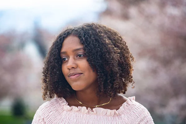 Charming Beautiful Black teen girl with big curly hair. Thinking and being contemplative. Outdoor candid portrait of a natural beauty. Spring Blossoms portrait