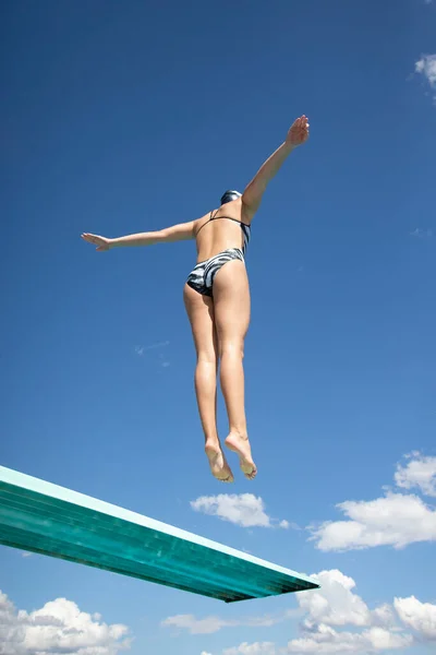 从下面看合适的女人从跳板跳高跳进游泳池 背景为蓝天云彩的抽象图像 大量的复制空间 — 图库照片