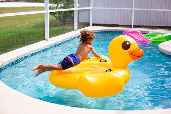 Young Diverse Little Boy Jumping Large Inflatable Pool Toy Backyard Stockfoto