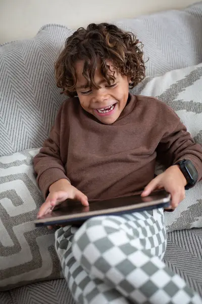 快乐的小男孩在家里的平板电脑上玩着一个有趣的电子游戏 一边笑着 不同的孩子把他的闲暇时间花在屏幕上 青少年的屏幕时间概念 图库图片