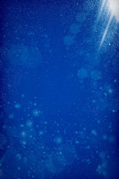 鮮やかな青色の背景に浮かぶ粉塵粒子 白い塵の質および明るい光線のビームが通って来ます ボケ光線を用いたテクスチャーブルーの背景 ストック写真