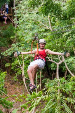 Kosta Rika 'da tatildeyken orman macerasından zevk alan gülümseyen bir kadın. Manzaralı bir dağdan aşağı inerken kollarını aç.