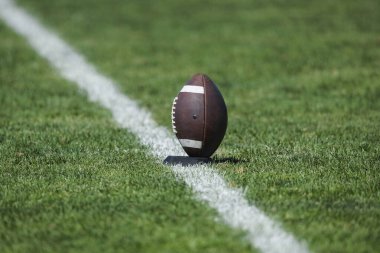 Amerikan futbolu bir golf sahasında dinleniyor ve bir futbol maçına başlamak için tekmelenmeye hazır. Futbol maçı başlamaya hazır. Başlama zamanı.