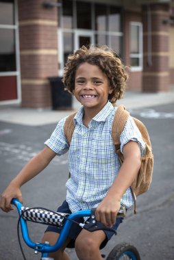 Günün sonunda bisikletle okuldan ayrılan çok tatlı, genç bir ilkokul öğrencisi. Eve döndüğüm için mutluyum. Harika eğitim fotoğrafı.