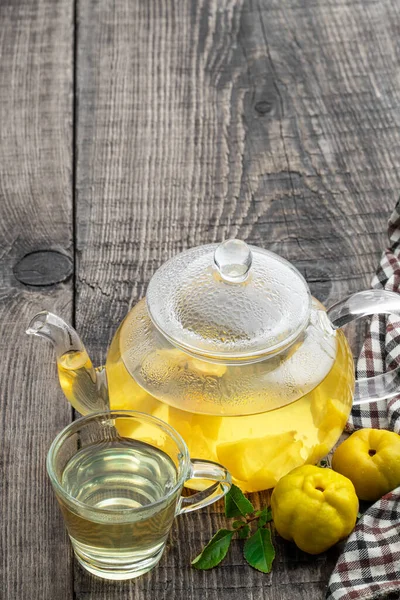 Hot quince  tea in transparent teapot with fresh fruits on wooden table