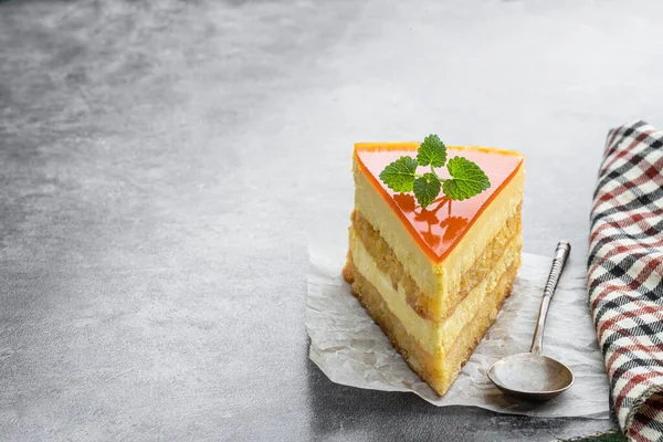 Slice  of layered mango cheesecake on gray background