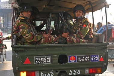 Bangladeş Ordusu personeli, 5 Ocak 2024 tarihinde Bangladeş 'in Dhaka kentinde yapılacak 12. Genel Seçimler için bir caddede devriye gezerken bir aracın arkasında oturuyor. Seçim güvenlik görevleri, barışçıl bir atmosfer ve durgunluğun sağlanmasına yardımcı olmaya başladı