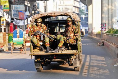 Bangladeş Ordusu personeli, 5 Ocak 2024 tarihinde Bangladeş 'in Dhaka kentinde yapılacak 12. Genel Seçimler için bir caddede devriye gezerken bir aracın arkasında oturuyor. Seçim güvenlik görevleri, barışçıl bir atmosfer ve durgunluğun sağlanmasına yardımcı olmaya başladı