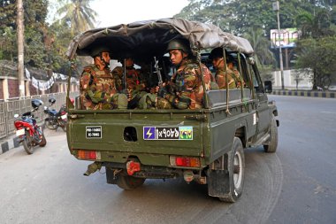 Bangladeş Ordusu personeli, 5 Ocak 2024 tarihinde Bangladeş 'in Dhaka kentinde yapılacak 12. Genel Seçimler için bir caddede devriye gezerken bir aracın arkasında oturuyor. Seçim güvenlik görevleri, barışçıl bir atmosfer ve durgunluğun sağlanmasına yardımcı olmaya başladı