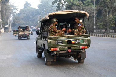 Bangladeş Ordusu personeli, 5 Ocak 2024 tarihinde Bangladeş 'in Dhaka kentinde yapılacak 12. Genel Seçimler için bir caddede devriye gezerken bir aracın arkasında oturuyor. Seçim güvenlik görevleri, barışçıl bir atmosfer ve durgunluğun sağlanmasına yardımcı olmaya başladı