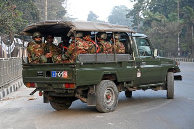 Bangladeş Ordusu personeli, 5 Ocak 2024 tarihinde Bangladeş 'in Dhaka kentinde yapılacak 12. Genel Seçimler için bir caddede devriye gezerken bir aracın arkasında oturuyor. Seçim güvenlik görevleri, barışçıl bir atmosfer ve durgunluğun sağlanmasına yardımcı olmaya başladı
