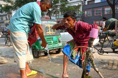 15 Nisan 2024 'te Bangladeş, Dhaka' da yüksek sıcaklıktaki bir günde yol kenarındaki bir su boru hattında yüzünü suyla yıkayan bir triportör sürücüsü.