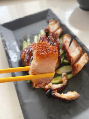 Çin usulü kavrulmuş domuz eti ya da Siu Yuk (kızarmış kızarmış domuz göbeği), bir çift çubuk tarafından toplanır.