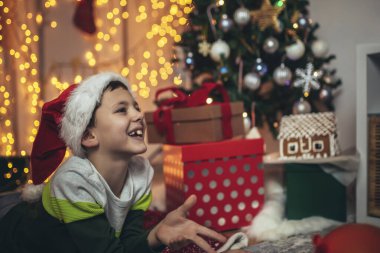 Mutlu çocuk, hediyelerle çevrili Noel ağacı önünde yerde yatıyor..