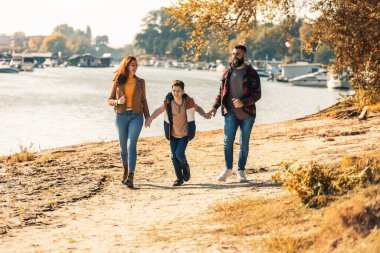 Ebeveynler ve oğulları nehir kenarında yürüyor kırsalda tatil yapıyorlar.