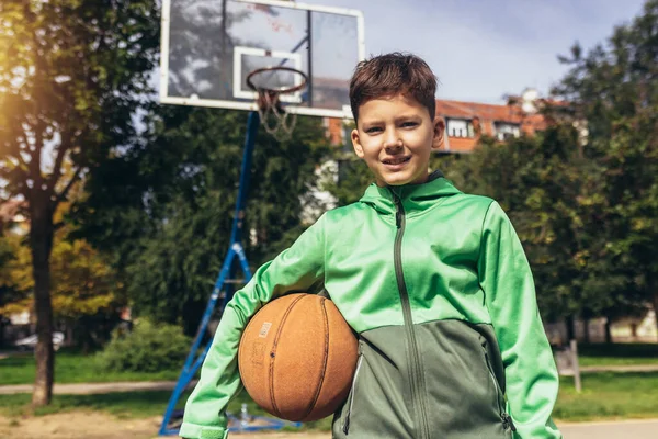 市内の遊び場でバスケットボールボールを保持緑のジャケットでかわいい男の子 — ストック写真