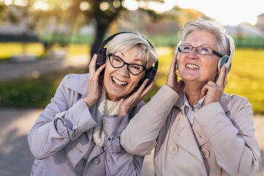 Doğada müzik dinleyen üst düzey bayan arkadaşlar, parkta cep telefonuyla müzik dinleyen kadınlar..