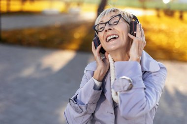 Doğada müzik dinleyen yaşlı bir kadın, parkta cep telefonuyla müzik dinleyen bir kadın.