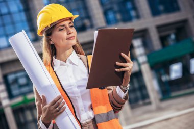 Güvenlik ekipmanlarında çalışan mühendis kadın planları tutuyor. İnşa, geliştirme, inşaat ve mimari kavramı.