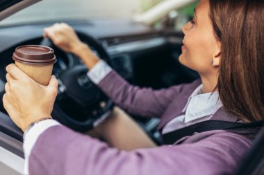 Genç bir iş kadını işe arabayla gidiyor, kahve içiyor..