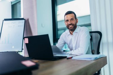 Ofisteki masasında dizüstü bilgisayarla oturan genç bir iş adamının portresi.