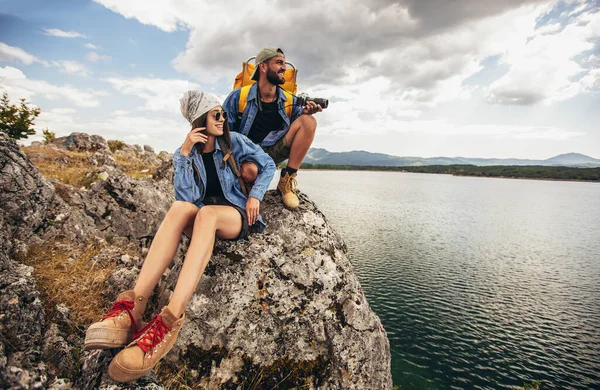 山の湖で楽しむ崖の上に座っているバックパック付きのハイカー — ストック写真