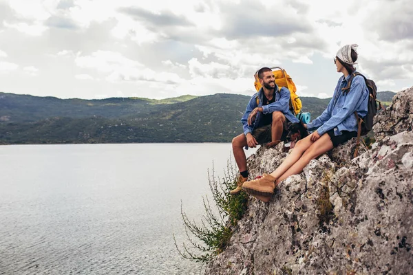 山で楽しむ崖の上に座っているバックパックと彼らのDobermanを持つハイカー — ストック写真