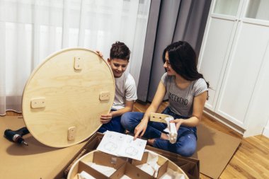 Erkek kardeş ve kız kardeş günlük kıyafetlerle evde mobilya monte ediyorlar. 