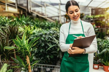 Çiçekçide çalışan mutlu küçük işletme sahibi kadın bitkilerle çevrili duruyor.