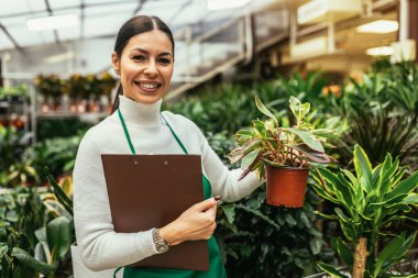 Çiçekçide çalışan mutlu küçük işletme sahibi kadın bitkilerle çevrili duruyor.