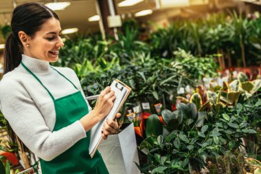 Çiçekçide çalışan mutlu küçük işletme sahibi kadın bitkilerle çevrili duruyor.