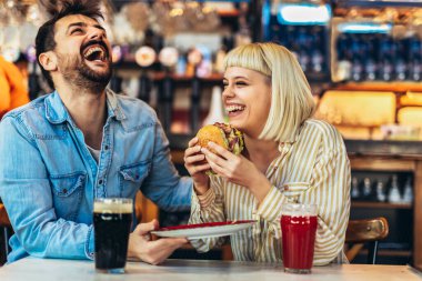 Genç aşıklar restoranda vakit geçirip, hamburger yiyip, bira içerek eğleniyorlar.