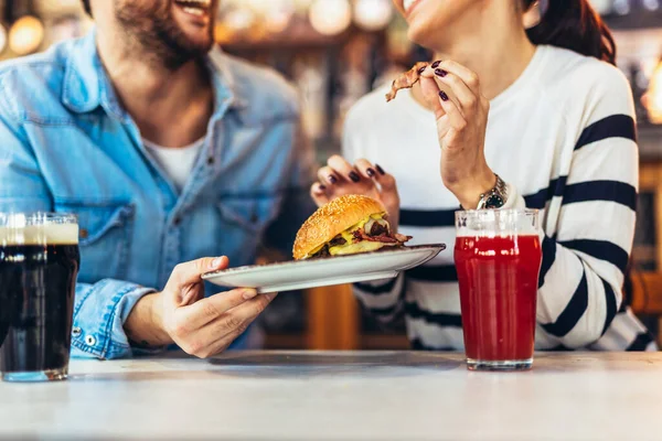 Young couple in love having fun spending leisure time together at restaurant, eating burgers and drinking beer