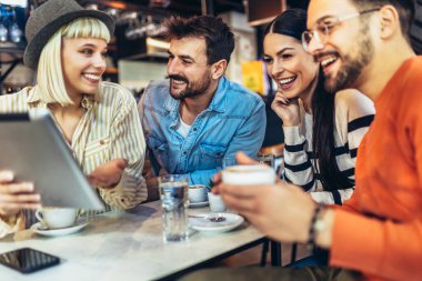 Kafede otururken dijital tablete bakan genç arkadaşlar. 