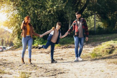 Ebeveynler ve oğulları nehir kenarında yürüyor kırsalda tatil yapıyorlar.