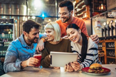 Kafede otururken dijital tablete bakan genç arkadaşlar. 