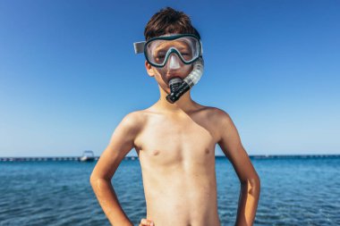 Deniz kenarında dalgıç maskeli gülümseyen küçük bir çocuğun portresi.