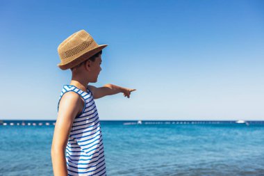 Kumsaldaki şapkalı mutlu çocuk deniz ufkuna bakıyor.